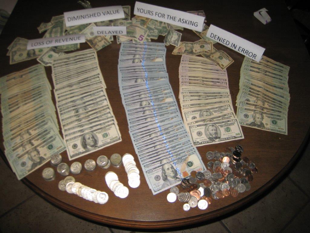 Bill Cook’s photograph of money spread across a table, with labels for loss of revenue, diminished value, delayed claims, and claims denied in error.